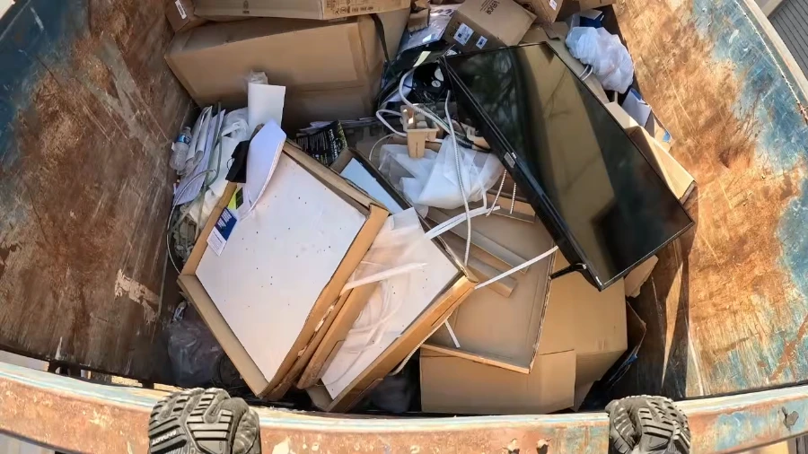 Old TV, electronics and cardboard boxes inside a roll-off dumpster