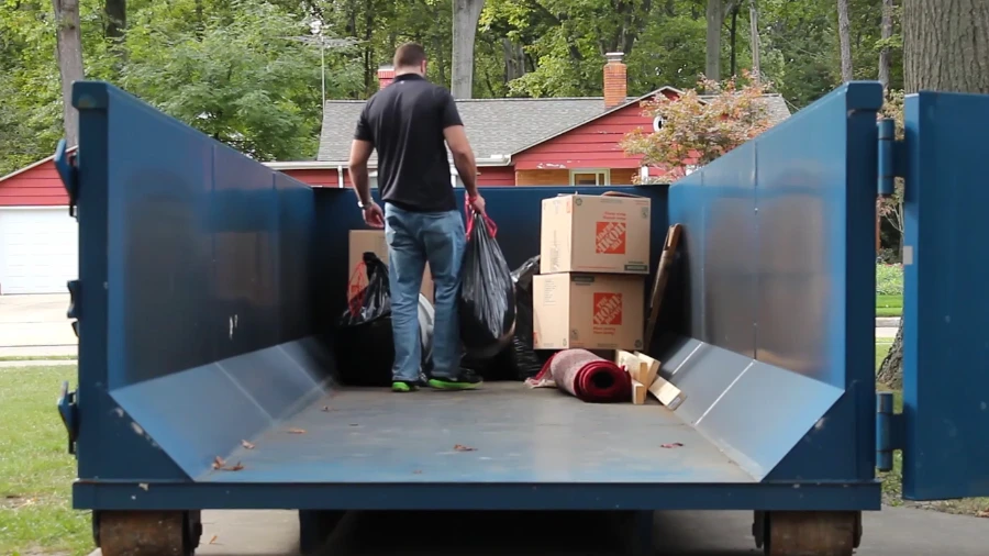 Man carrying boxes through the open swing door of a walk-in roll-off dumpster during a home cleanout